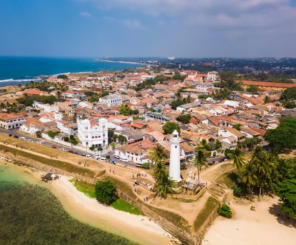 Aerial view of Galle, Sri Lanka, featuring a colonial-styled coastal town, a white lighthouse, and lush palm trees near the shoreline.