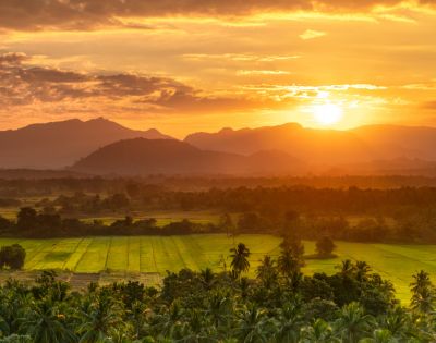 A breathtaking sunset over lush green fields and distant mountains, casting warm golden hues across the landscape.