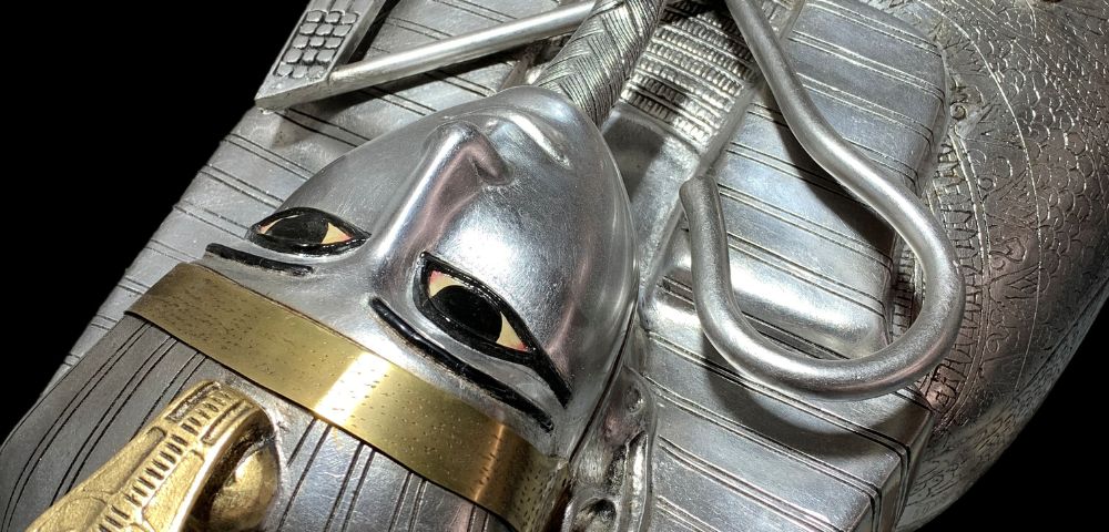 Close-up of a silver sarcophagus with a stylized human face, gold accents, and intricate engravings, showcasing ancient Egyptian artistry.