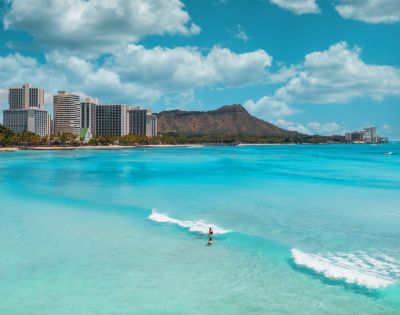 A vibrant beach scene in Honolulu, Hawaii, showcasing turquoise waters, surfers, and the iconic Diamond Head mountain in the background.