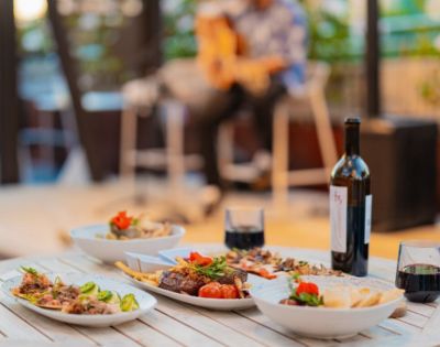 Dining table with a variety of dishes, red wine, and glasses, with a musician playing guitar in the background.
