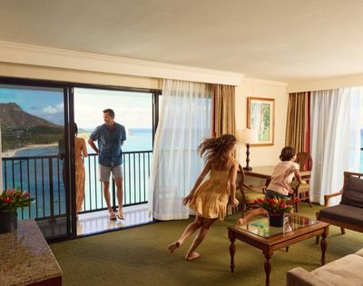 A vibrant hotel room with a stunning ocean view; two people enjoying the moment, while a third stands by the balcony.