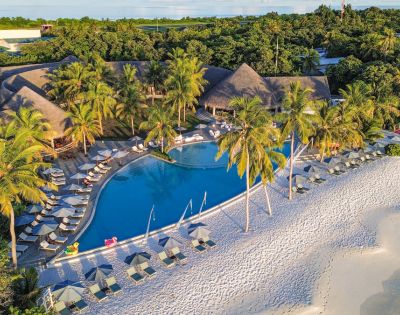 Aerial view of a tropical resort with a swimming pool, palm trees, and a sandy beach, surrounded by lush greenery and colorful cabanas.
