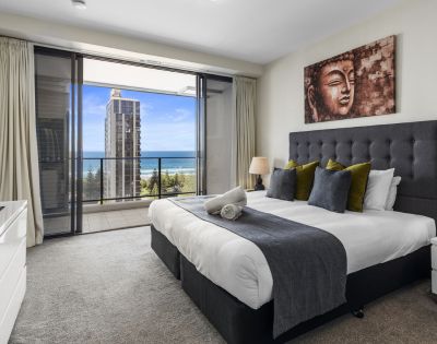 A modern bedroom featuring a large bed with decorative pillows, a TV, and a stunning view of the ocean through large sliding doors.
