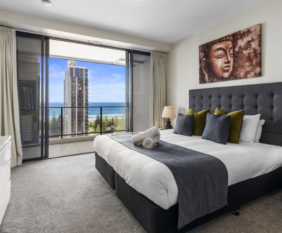 A modern bedroom featuring a large bed with decorative pillows, a TV, and a stunning view of the ocean through large sliding doors.