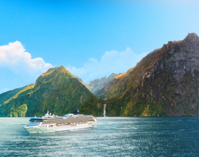 A cruise ship sails through tranquil waters, surrounded by towering green mountains and a cascading waterfall under a clear blue sky.