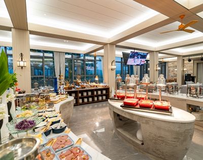 A spacious buffet spread with various dishes, glassware, and decorative plants, illuminated by warm lighting in a modern dining area.