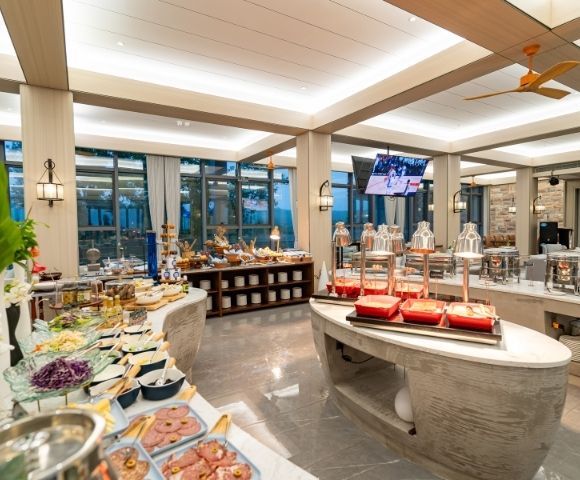 A spacious buffet spread with various dishes, glassware, and decorative plants, illuminated by warm lighting in a modern dining area.