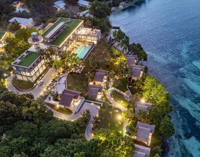 Aerial view of a luxurious seaside resort with glowing lights, lush greenery, and a turquoise ocean, showcasing stunning architecture.