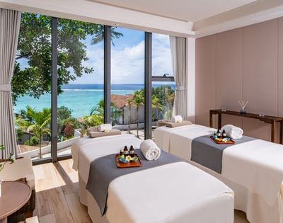A serene spa room with two massage tables, ocean views, and tropical decor, inviting relaxation and tranquility.