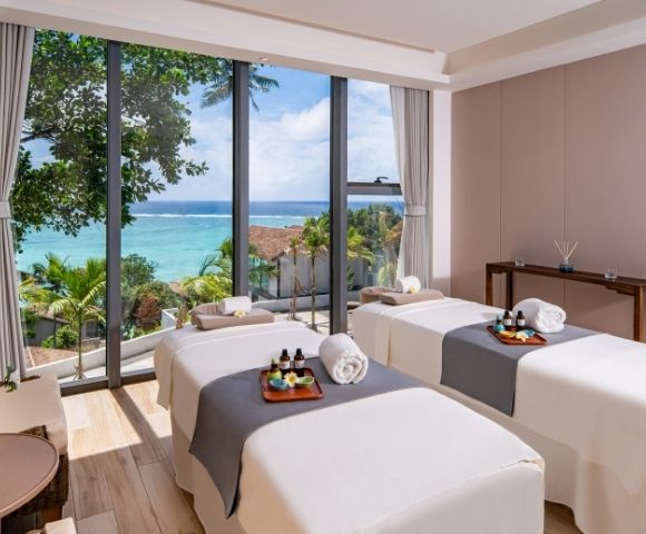 A serene spa room with two massage tables, ocean views, and tropical decor, inviting relaxation and tranquility.