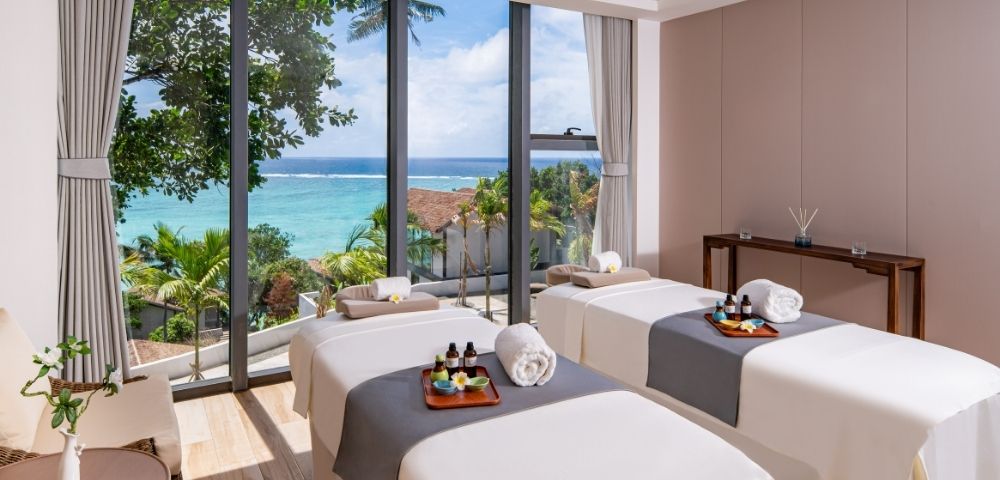 A serene spa room with two massage tables, ocean views, and tropical decor, inviting relaxation and tranquility.