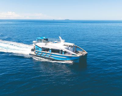 A sleek, white and blue catamaran, named Lynx, speeds across blue waters under a clear sky, leaving a frothy wake behind.