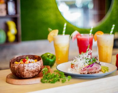 Colorful tropical drinks and fresh dishes served in wooden bowls, showcasing vibrant ingredients in a bright restaurant setting.