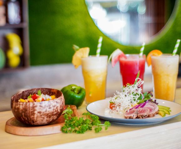Colorful tropical drinks and fresh dishes served in wooden bowls, showcasing vibrant ingredients in a bright restaurant setting.