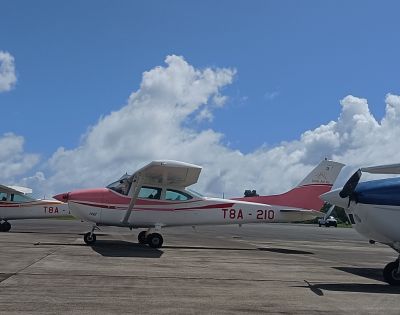 A Cessna aircraft with a red and white design, parked on a tarmac under a blue sky with fluffy clouds.