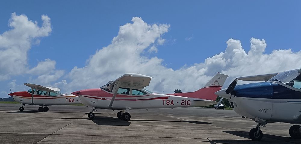 A Cessna aircraft with a red and white design, parked on a tarmac under a blue sky with fluffy clouds.
