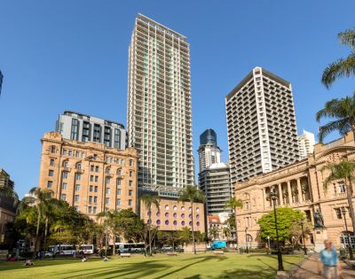 A vibrant cityscape featuring modern skyscrapers alongside historic buildings, with green space in the foreground under a clear blue sky.