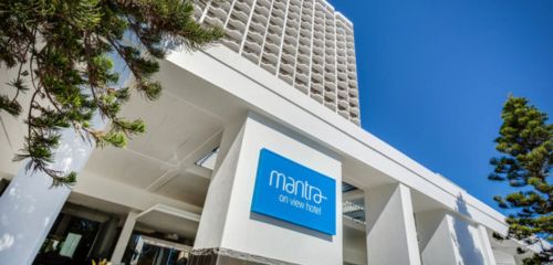 Exterior view of the Mantra On View Hotel, showcasing modern architecture and a clear blue sky. Green foliage in the foreground.