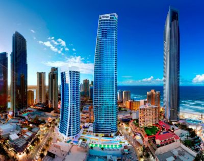 Image displays a harmonious blend of modern and traditional cityscape. The images focal point is a towering blue skyscraper, while the sea and sky provide a stunning backdrop. The red-roofed and diverse architectural details create a lively urban scene, captured in a serene and visually appealing composition.