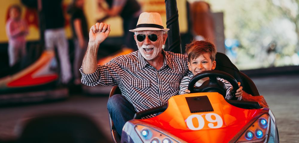An adult and a child excitedly ride in a colorful bumper car at an amusement park.