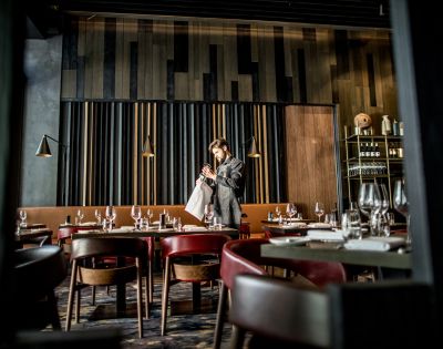 A stylish modern restaurant interior with dark wooden panels and shelves filled with bottles and glasses in the background.