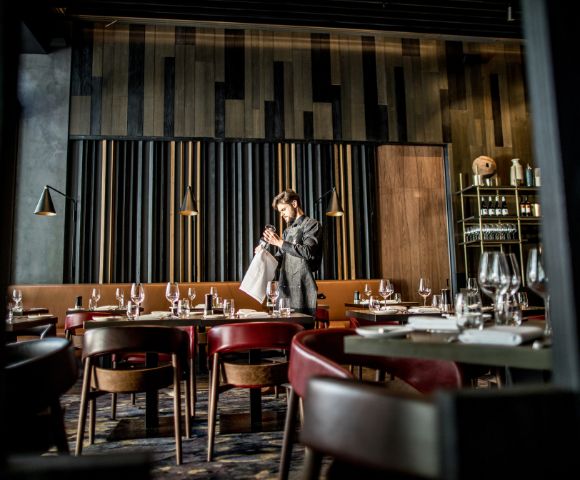 A stylish modern restaurant interior with dark wooden panels and shelves filled with bottles and glasses in the background.