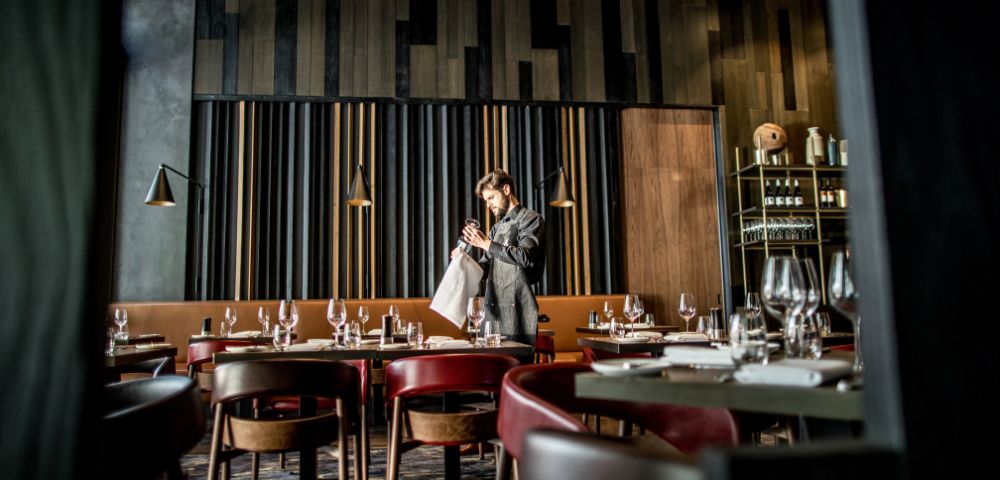 A stylish modern restaurant interior with dark wooden panels and shelves filled with bottles and glasses in the background.