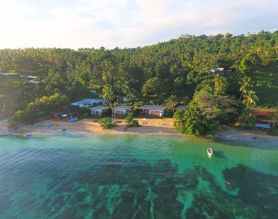 Aerial view of a tranquil beach with cabins, surrounded by palm trees and clear turquoise water, ideal for relaxation and leisure.