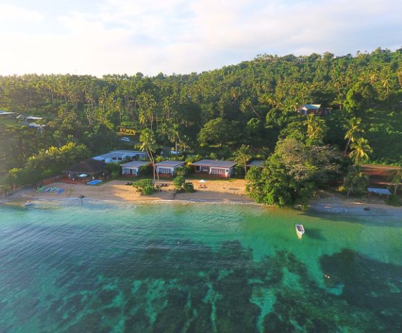Aerial view of a tranquil beach with cabins, surrounded by palm trees and clear turquoise water, ideal for relaxation and leisure.