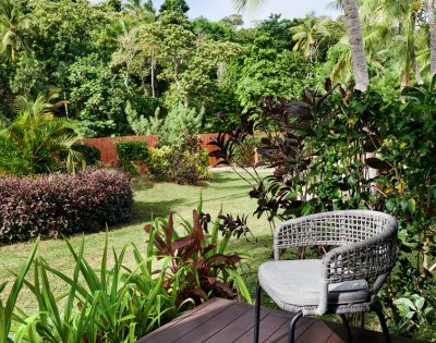 A cozy outdoor chair on a deck, surrounded by lush greenery and tropical plants, overlooking a tranquil garden landscape.