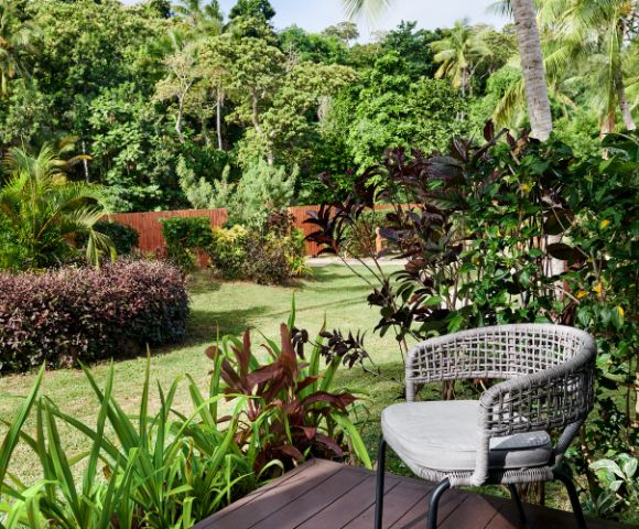 A cozy outdoor chair on a deck, surrounded by lush greenery and tropical plants, overlooking a tranquil garden landscape.