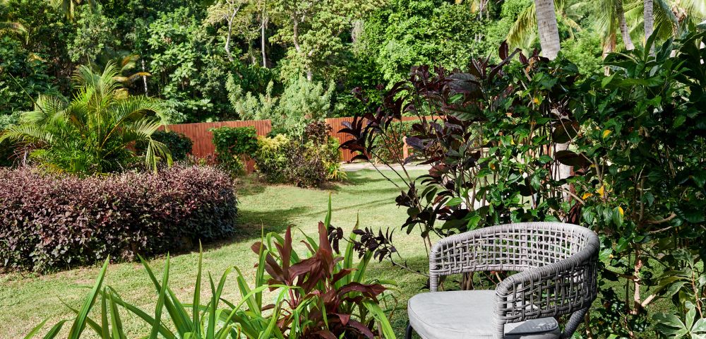A cozy outdoor chair on a deck, surrounded by lush greenery and tropical plants, overlooking a tranquil garden landscape.