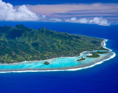 Aerial view of a lush, green island with turquoise waters, white sandy beaches, and scattered rocky islets against a blue sky.