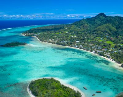 Aerial view of a tropical coastline featuring clear turquoise waters, lush green hills, and serene beachside communities.