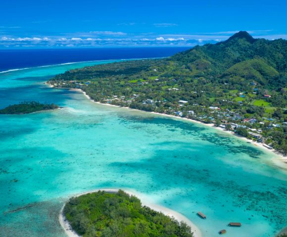 Aerial view of a tropical coastline featuring clear turquoise waters, lush green hills, and serene beachside communities.