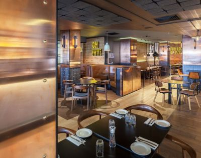 Modern restaurant interior with wooden floors, copper accents, and cozy leather booth seating. Warm ambiance, soft lighting, and neatly set tables.