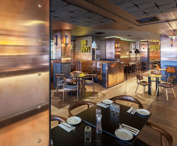 Modern restaurant interior with wooden floors, copper accents, and cozy leather booth seating. Warm ambiance, soft lighting, and neatly set tables.