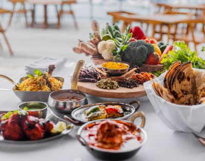 A vibrant spread of Indian cuisine on a table, featuring biryani, naan, and curries. Fresh vegetables, spices, and herbs add a colorful backdrop.