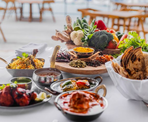 A vibrant spread of Indian cuisine on a table, featuring biryani, naan, and curries. Fresh vegetables, spices, and herbs add a colorful backdrop.