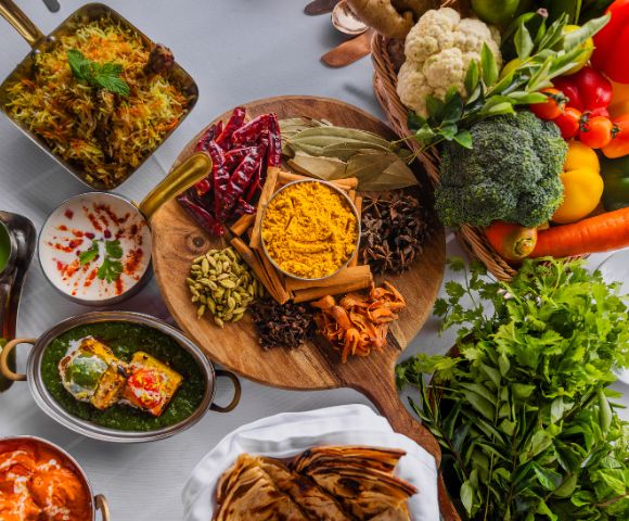 A vibrant display of Indian cuisine featuring colorful vegetables, spices on a wooden platter, and dishes like biryani and saag paneer, conveying richness.