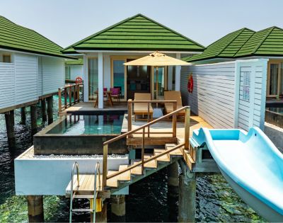 Luxurious overwater bungalows with green roofs, each featuring a private pool, sunbeds, and a blue slide leading to the ocean. A serene, tropical getaway.
