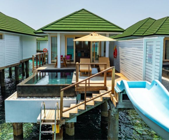 Luxurious overwater bungalows with green roofs, each featuring a private pool, sunbeds, and a blue slide leading to the ocean. A serene, tropical getaway.