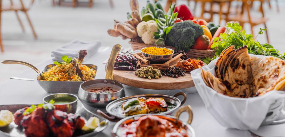 A vibrant spread of Indian cuisine on a table, featuring biryani, naan, and curries. Fresh vegetables, spices, and herbs add a colorful backdrop.