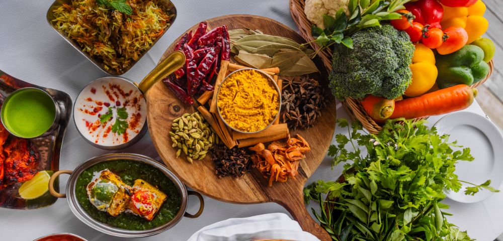 A vibrant display of Indian cuisine featuring colorful vegetables, spices on a wooden platter, and dishes like biryani and saag paneer, conveying richness.