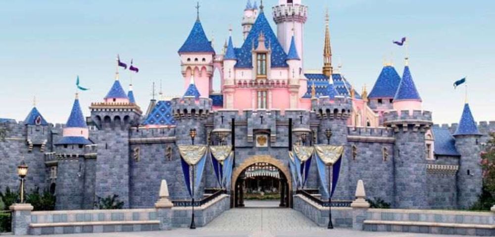 A pastel-colored fairy tale castle with blue turrets and pink walls, under a clear sky. Flags wave gently, evoking a magical, whimsical atmosphere.