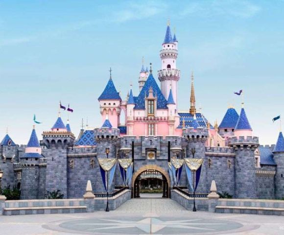 A pastel-colored fairy tale castle with blue turrets and pink walls, under a clear sky. Flags wave gently, evoking a magical, whimsical atmosphere.