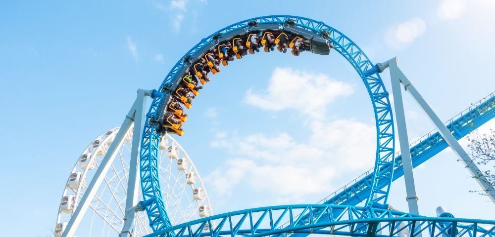 A roller coaster train twists through a blue loop, with excited riders silhouetted against a clear sky.