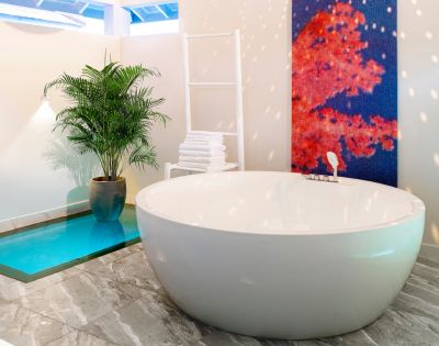 A modern bathroom with a large white oval bathtub, a tall potted plant, a white towel rack, and a vibrant red-blue abstract painting on the wall.