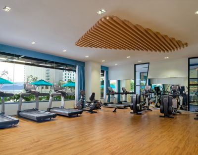 Spacious gym with wooden floors, six treadmills, and exercise bikes by large windows. Bright, modern design with a calm, inviting atmosphere.